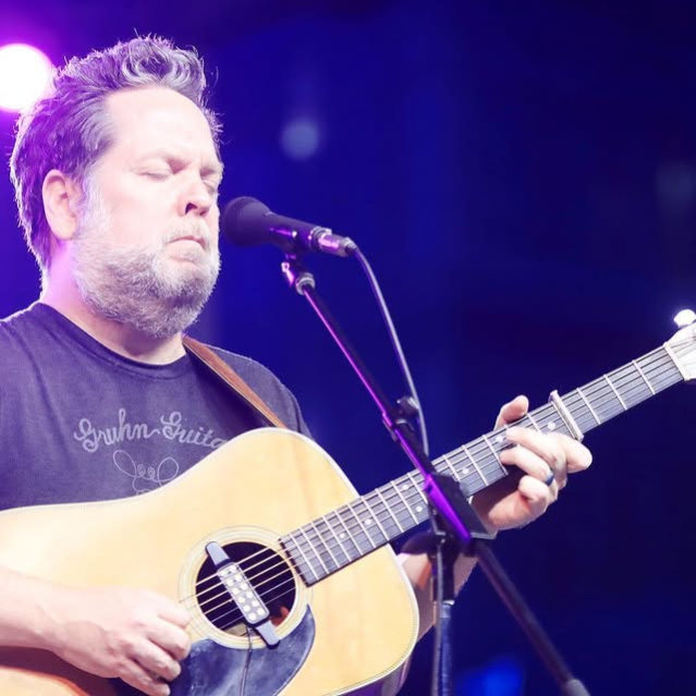 Chapman Welch singing and playing acoustic guitar on stage